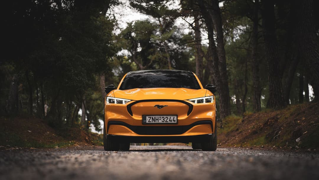 Front of a Ford Mustang Mach-e in mustard yellow in the forest