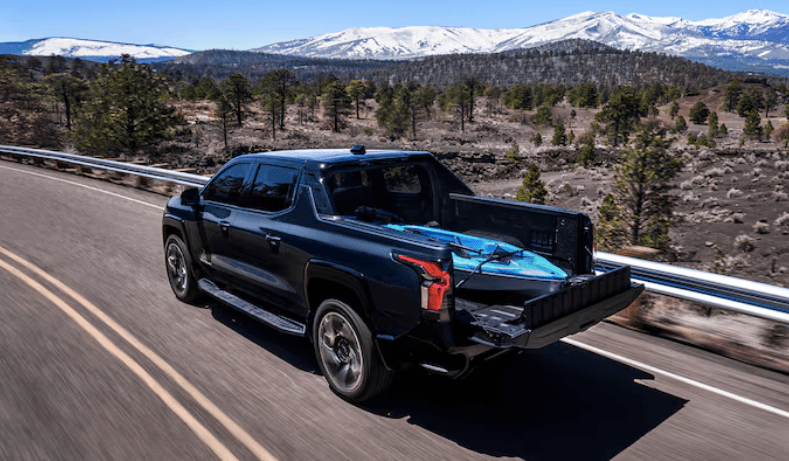 Chevrolet Silverado EV truck driving on highway with snowy mountains in background