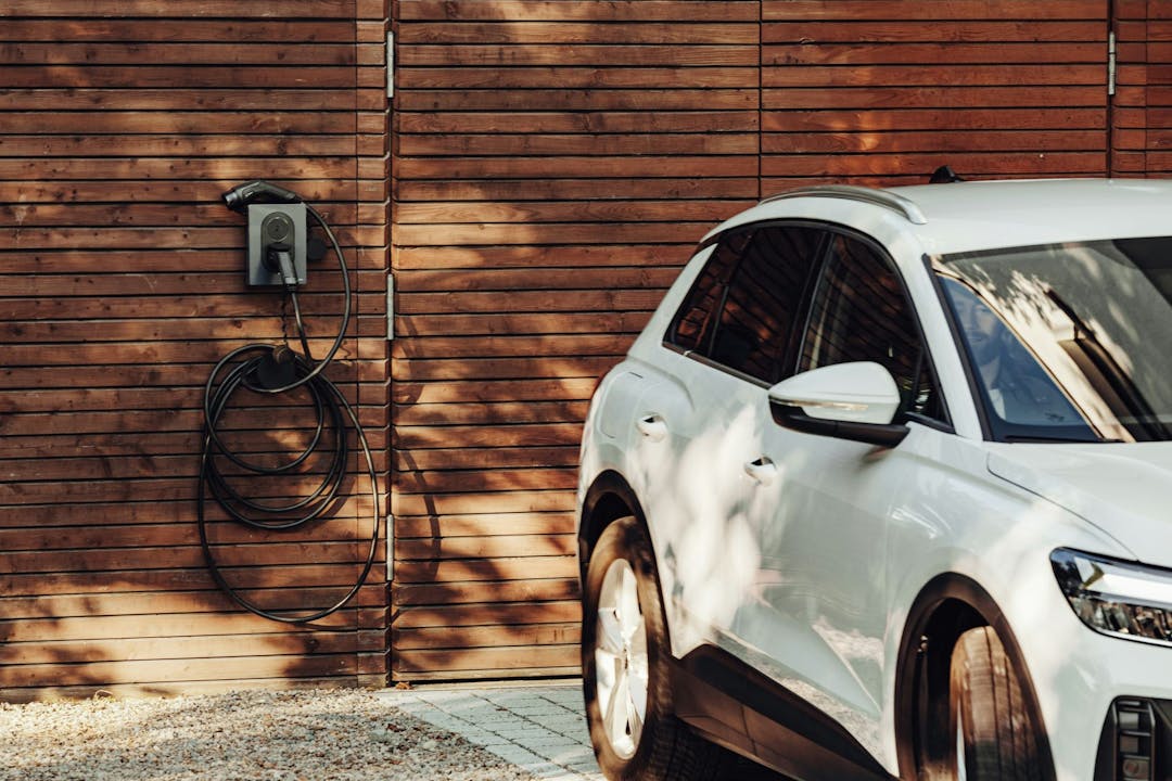 White EV parked outside garage with EV charger in background.